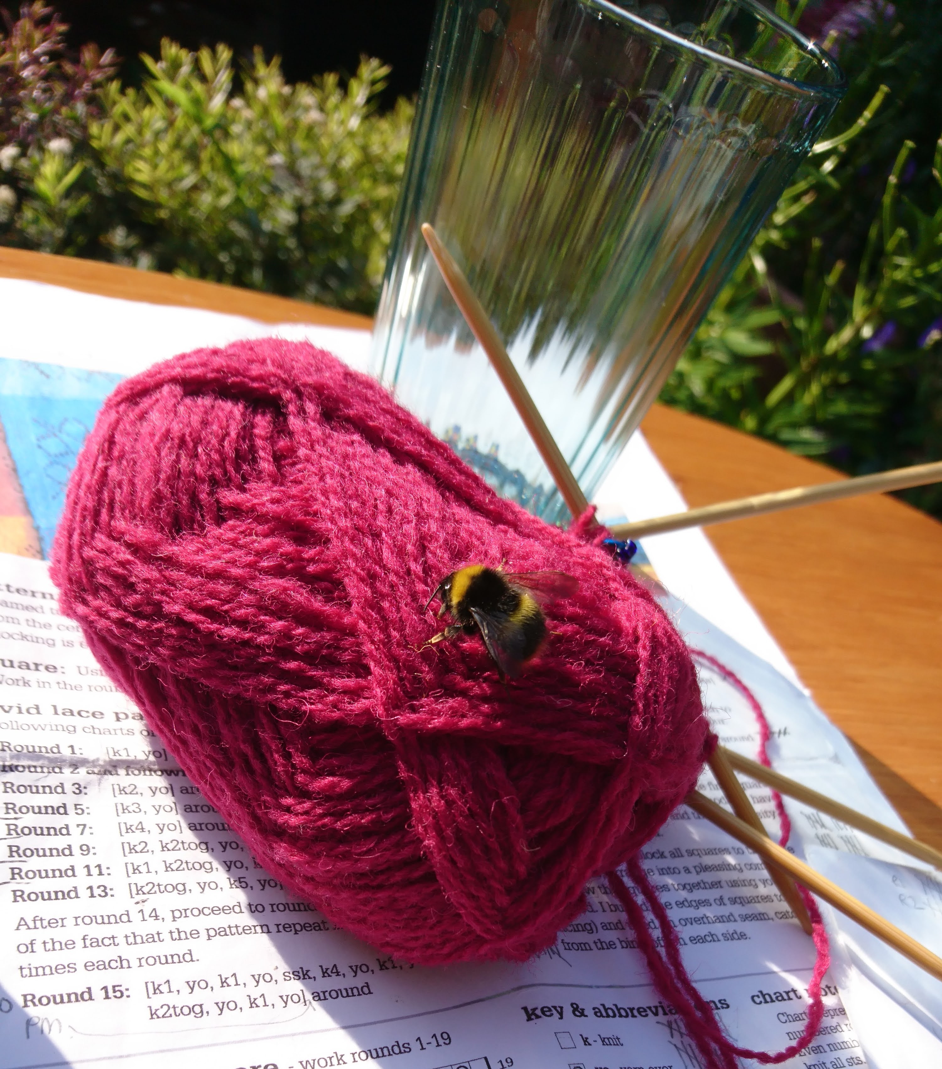 A bee on a burgundy coloured ball of wool outside in the garden. 